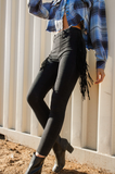 Person wearing black leggings with fringe details, standing against a white wall.