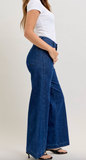 Person wearing blue wide-leg jeans and a white top on a plain background