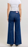 Person wearing blue jeans with a visible brand logo on a plain background